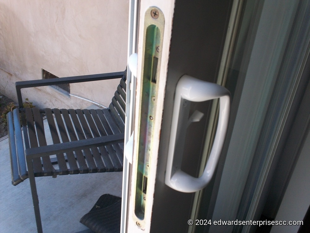 Door handle and latch, newly replaced. A black metal patio chair is visible just outside the door.